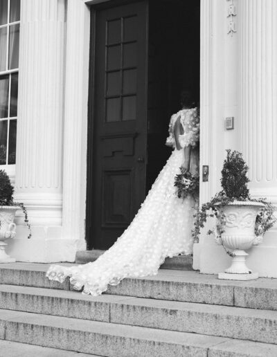 A black and white image of a bride entering her wedding venue.