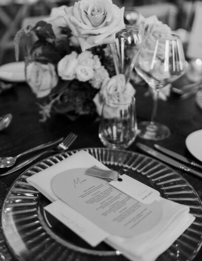 A black and white photo of a wedding table setting with a place card and personalised menu.