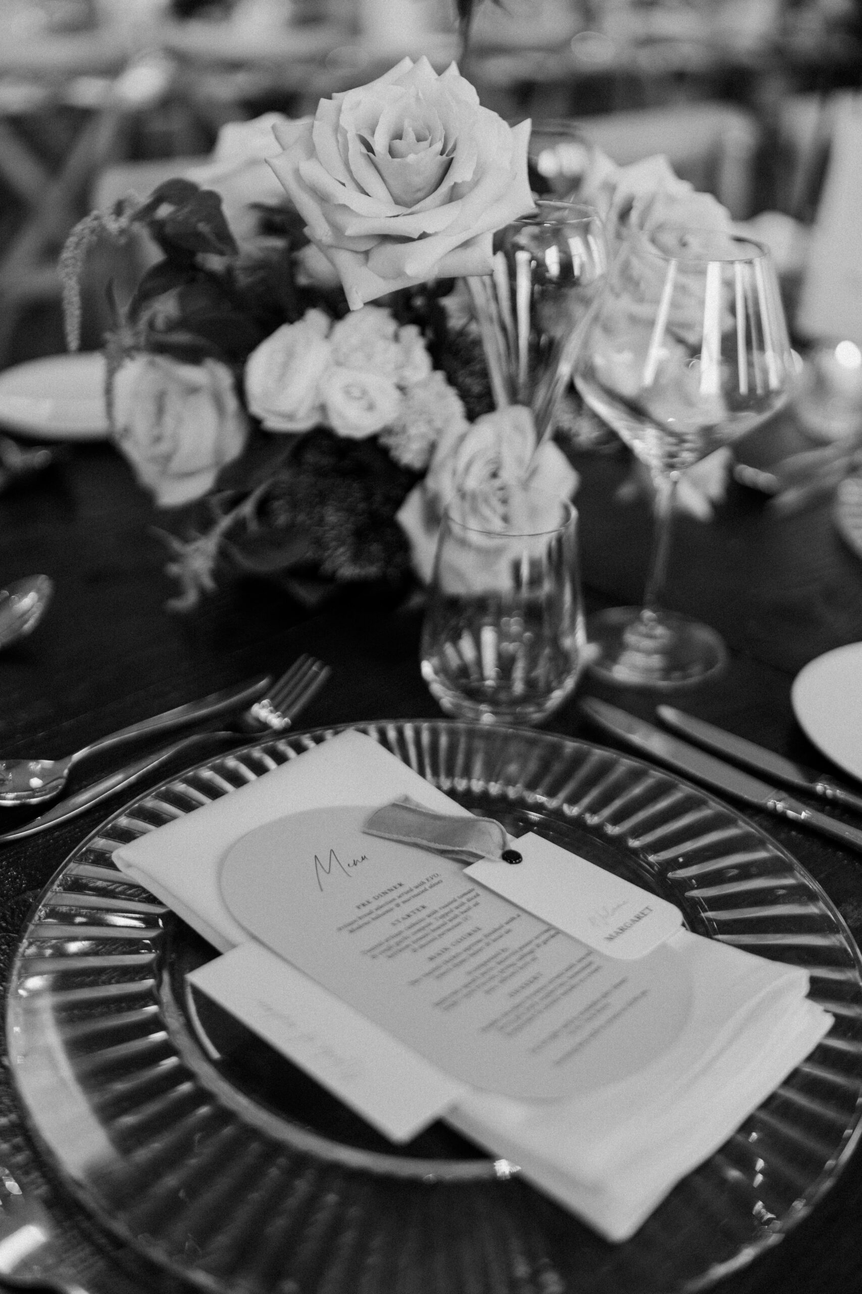 A black and white photo of a wedding table setting with a place card and personalised menu.