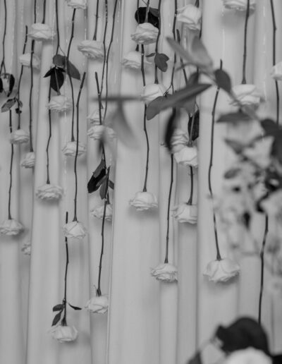 A black and white photo of a curtain styled with white roses delicately suspended from it to form a beautiful backdrop.