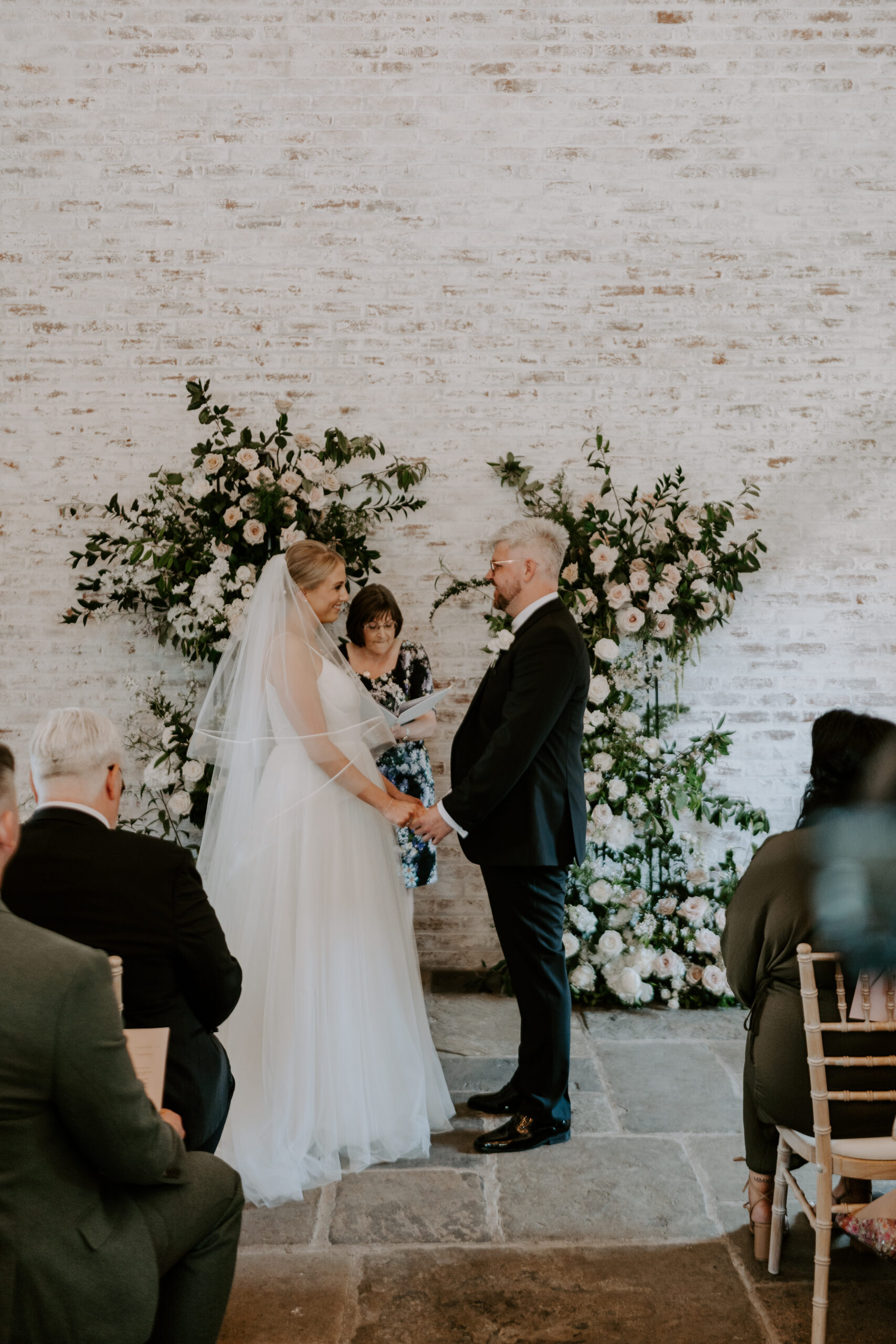 A bride and groom exchange vows during their beautifully styled wedding ceremony adorned with stunning flowers.