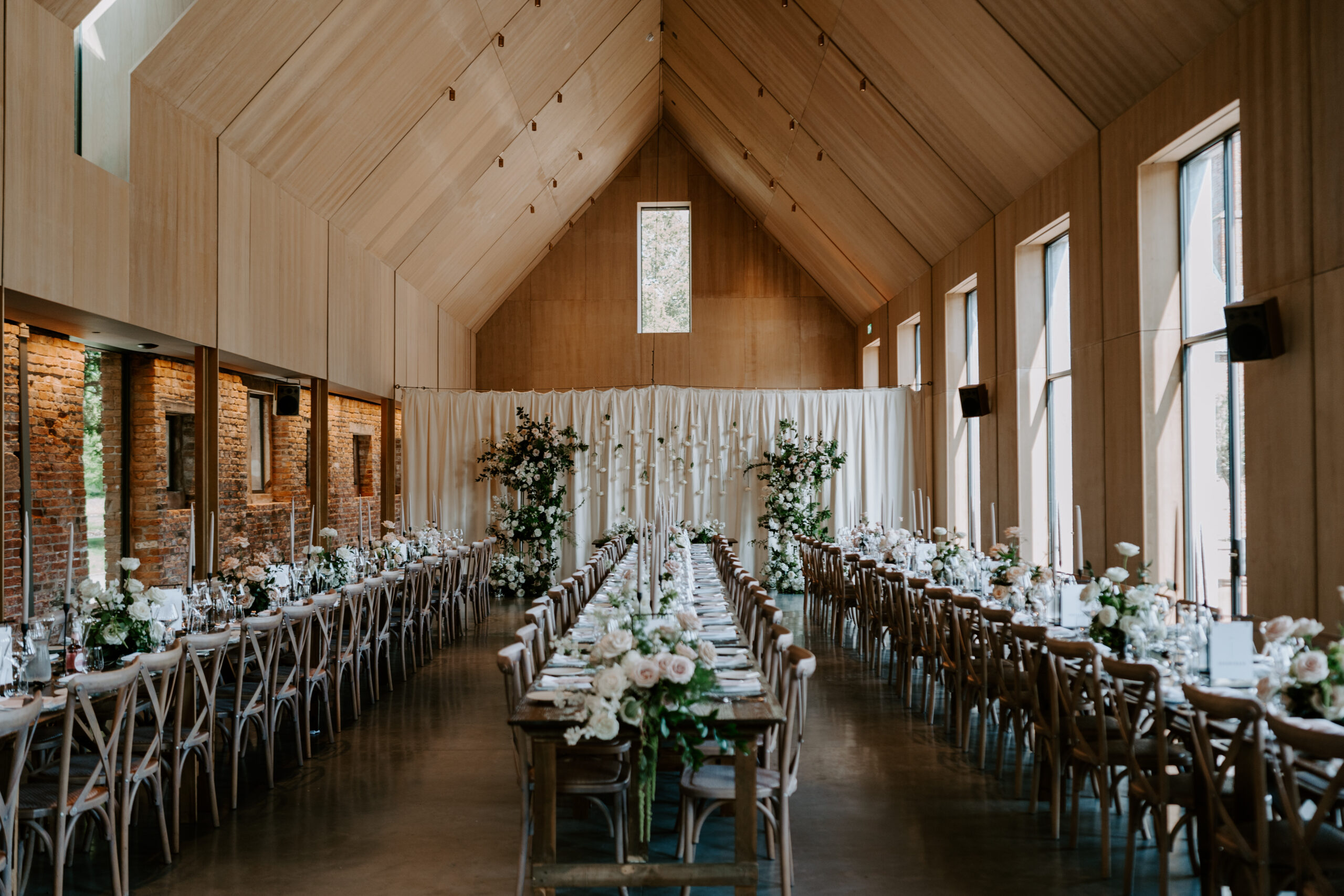 A colour photo showcasing long wedding tables styled with place settings and flowers, set in a hall.