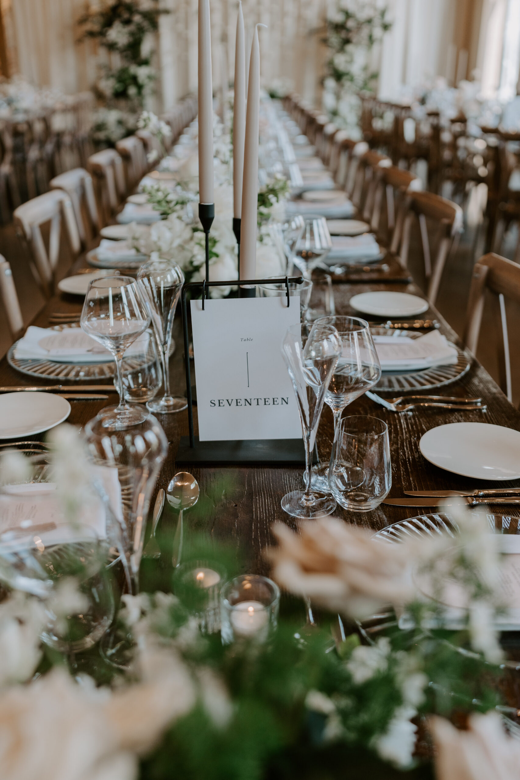 A beautifully styled long table with white flowers, candles and place settings and a table number card.