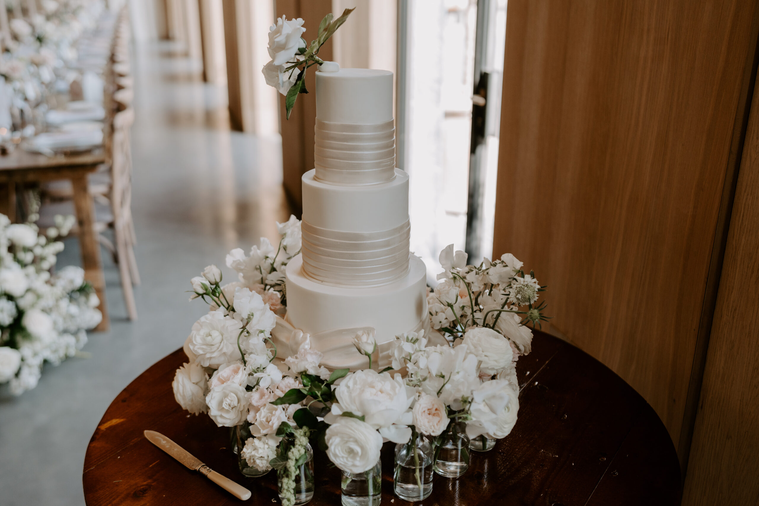 A white wedding cake surrounding with wedding flowers on a wooden table.