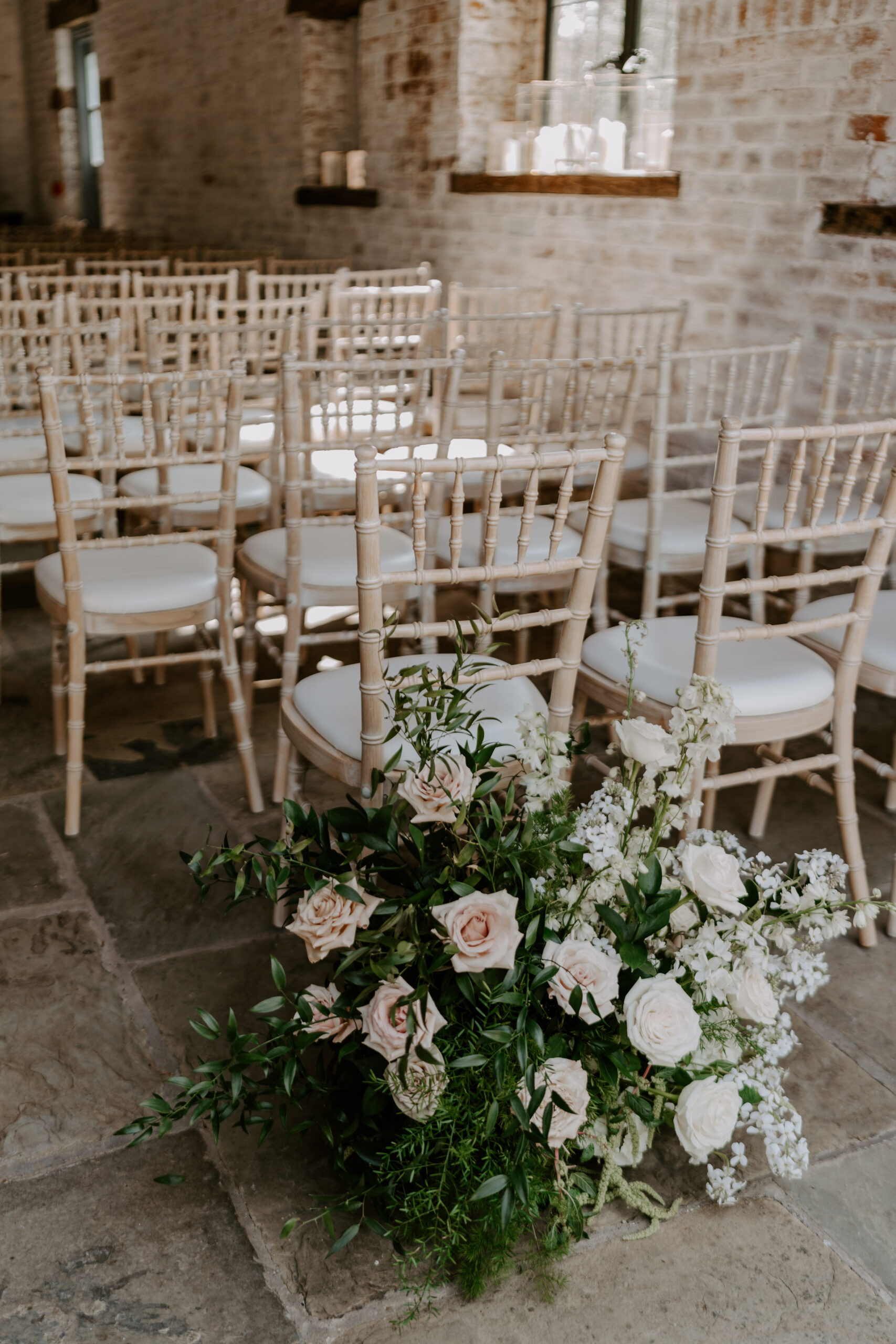 A large bouquet of pink and white roses and greenery sitting behind a row of chairs for a barn wedding.