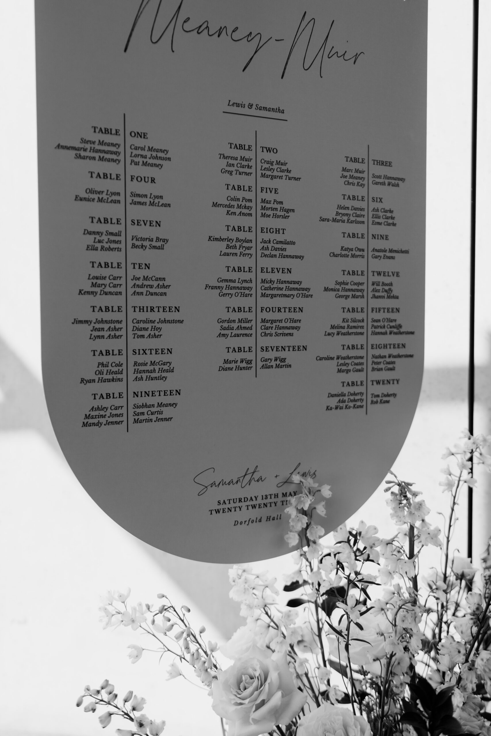 A black and white photo of a table plan with flowers in front of it, showcasing elegant wedding styling.