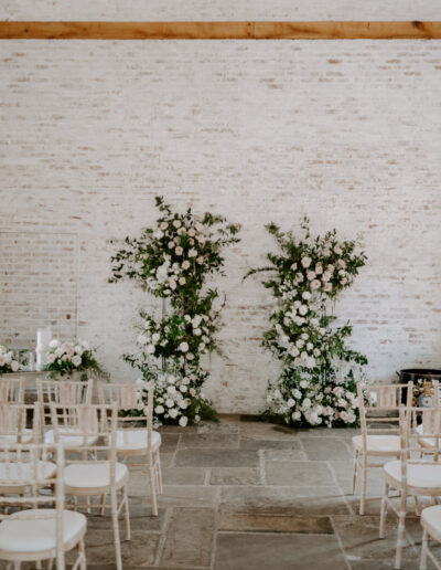 A barn wedding featuring pink and white flowers and chairs arranged either side of the aisle.