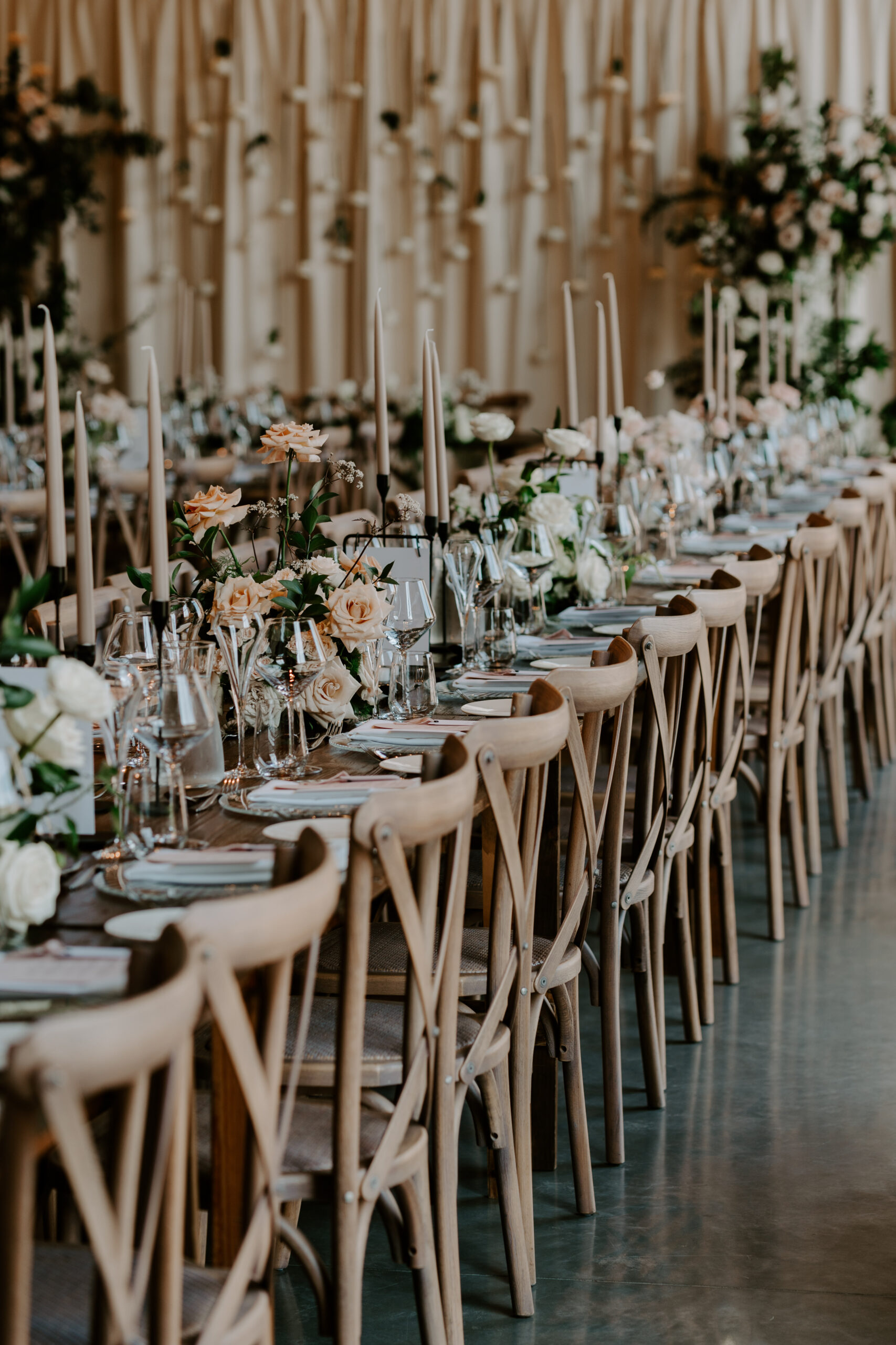 A wooden table set up with wedding styling and place settings, candles and flowers.