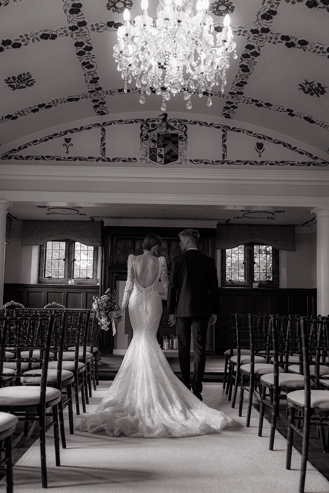 A black and white photo showcasing long wedding tables styled with place settings and flowers, set in a hall.