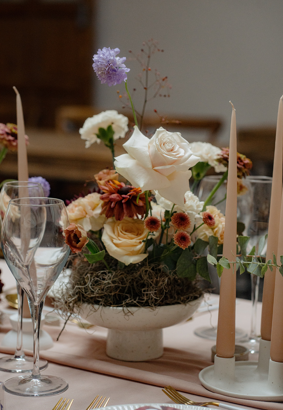 A beautifully styled long table with white flowers, candles and place settings and a table number card.