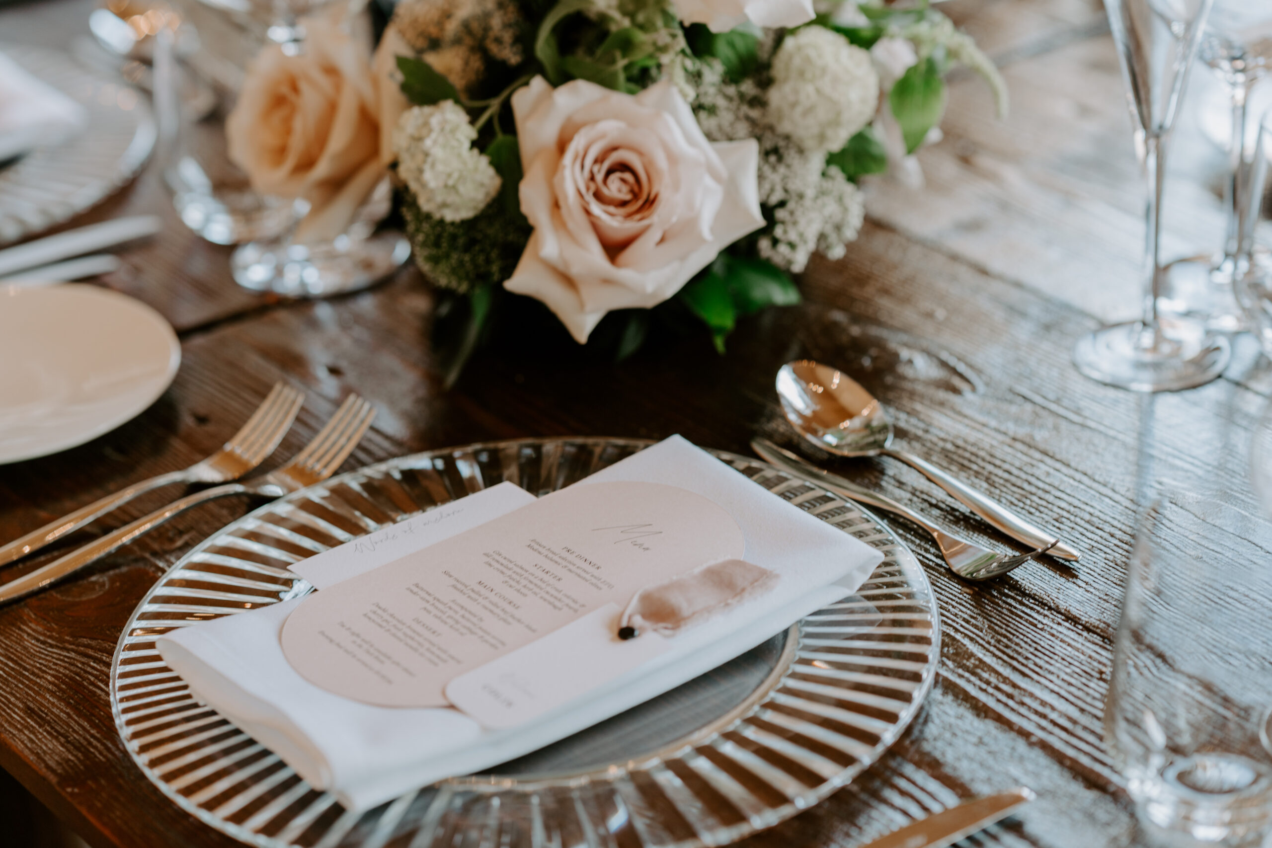 A black and white photo of a white wedding cake surrounding with wedding flowers on a wooden table.