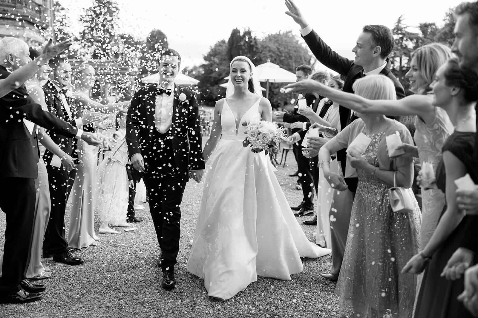 Madeleine & Chris A black and white image of a bride enjoying the confetti toss after their wedding ceremony at Capesthorne hall planned by Cheshire wedding planner Soiree Studio.