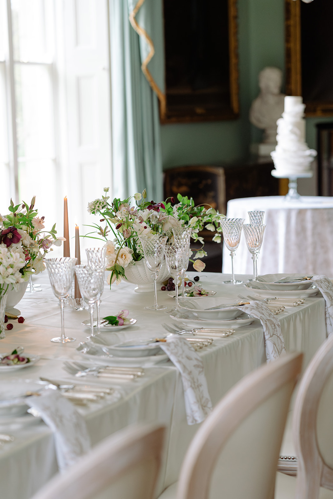 Birdsall House A colour image of a long top table at a wedding with neutral coloured table linens and a tall tiered cake in the background.
