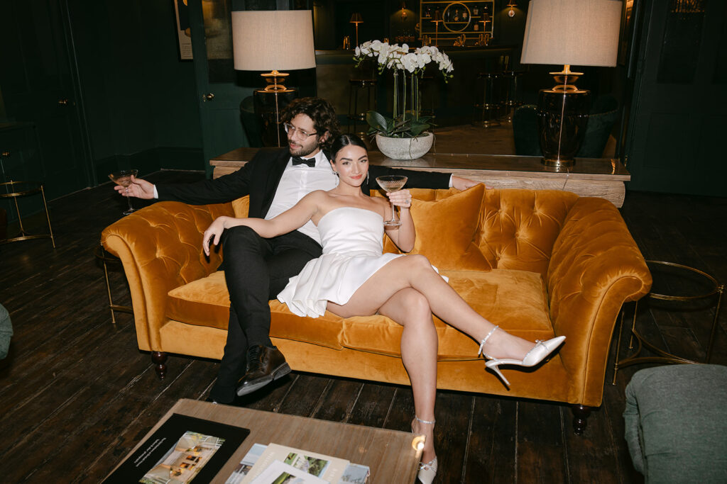 A bride and groom at Birdsall House in Yorkshire sat on the orange velvet couch in The Old Kitchens venue.