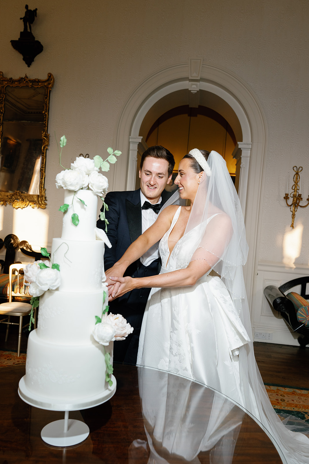 Madeleine & Chris A bride and groom cutting their three tier wedding cake adorned with sugar flowers on their wedding day.