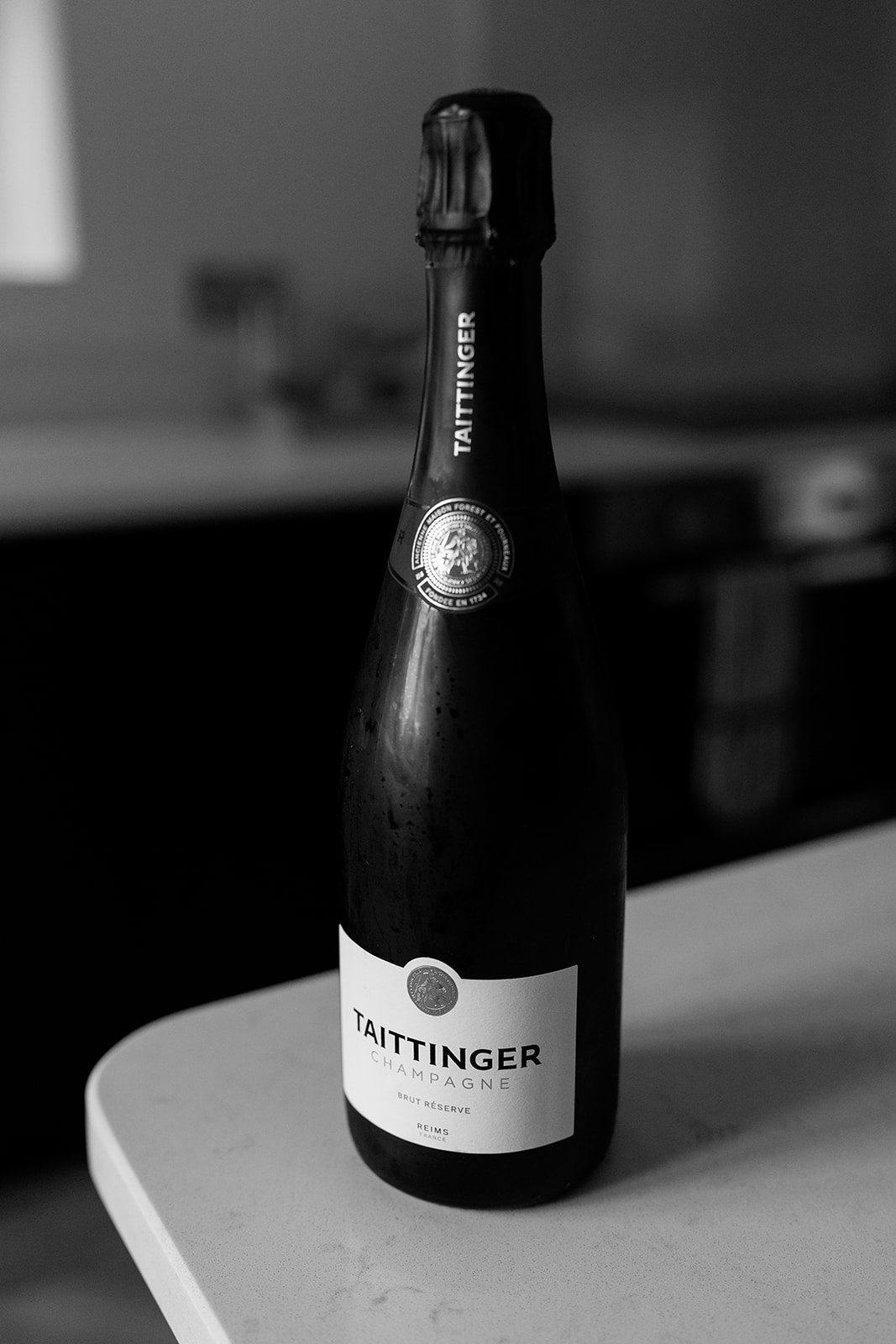 Madeleine & Chris A black and white image of a Taittinger champagne bottle at an evening marquee wedding reception in the Cotswolds.