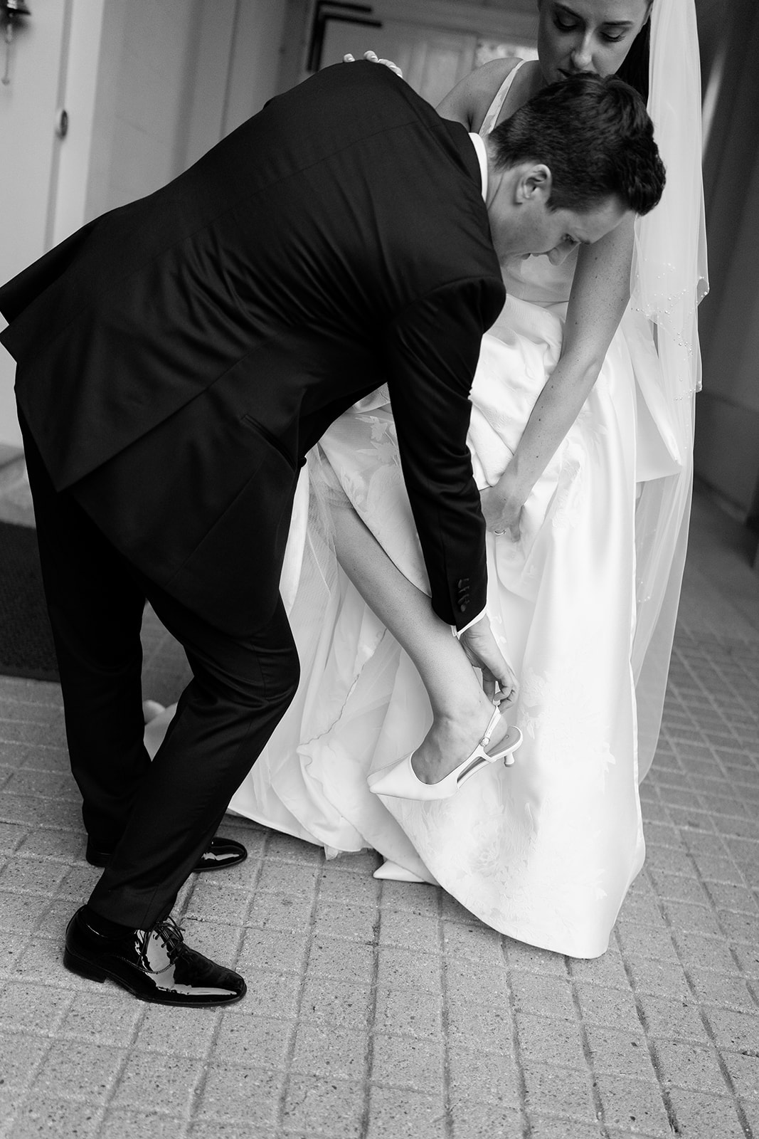 Madeleine & Chris A black and white editorial style wedding photography image of a groom helping his bride with her shoe.