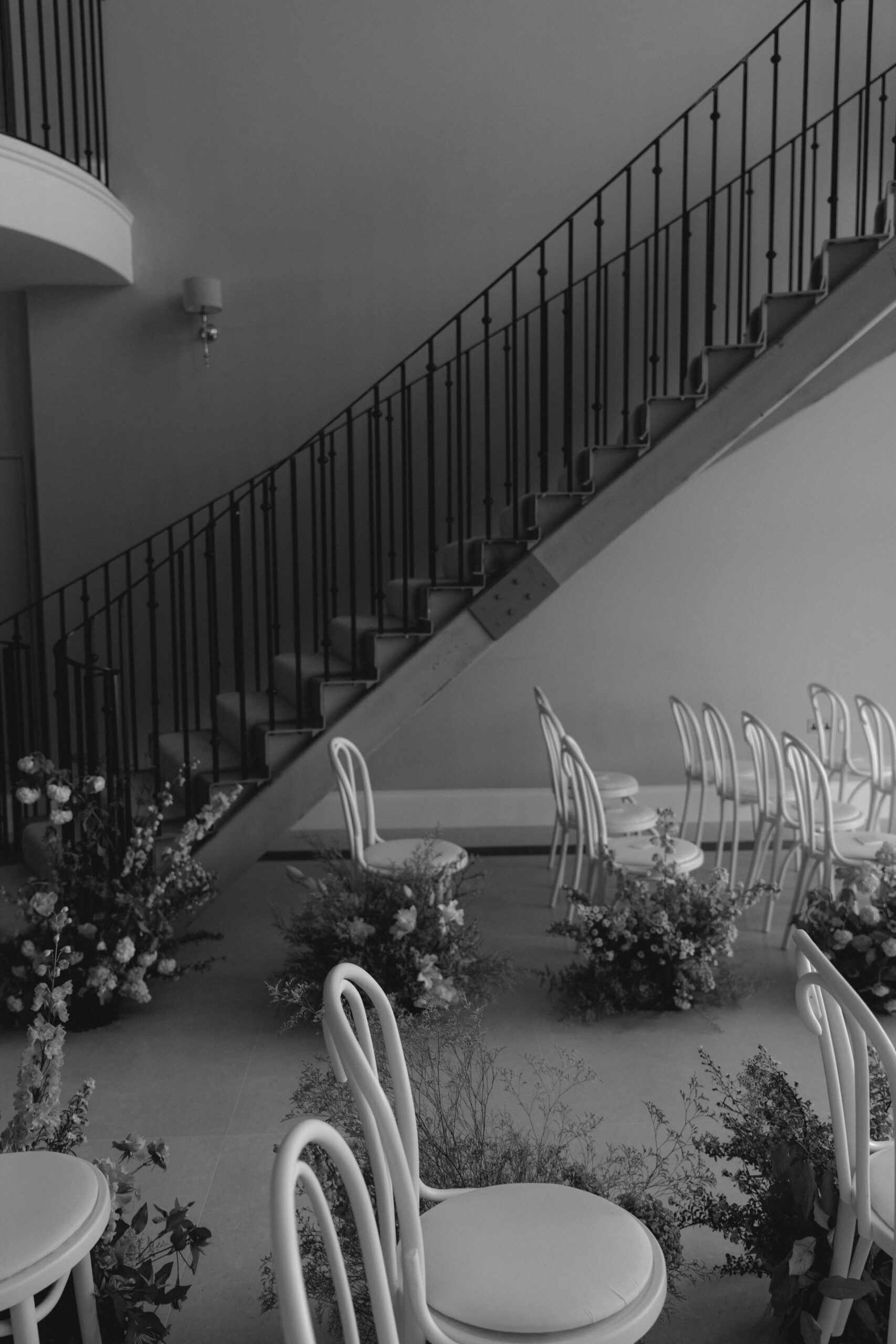 WEDDING-AISLE-COTSWOLDS-PLANNER A black and white image of a marquee wedding ceremony with white chairs and luxury aisle floristry by Sassflower.
