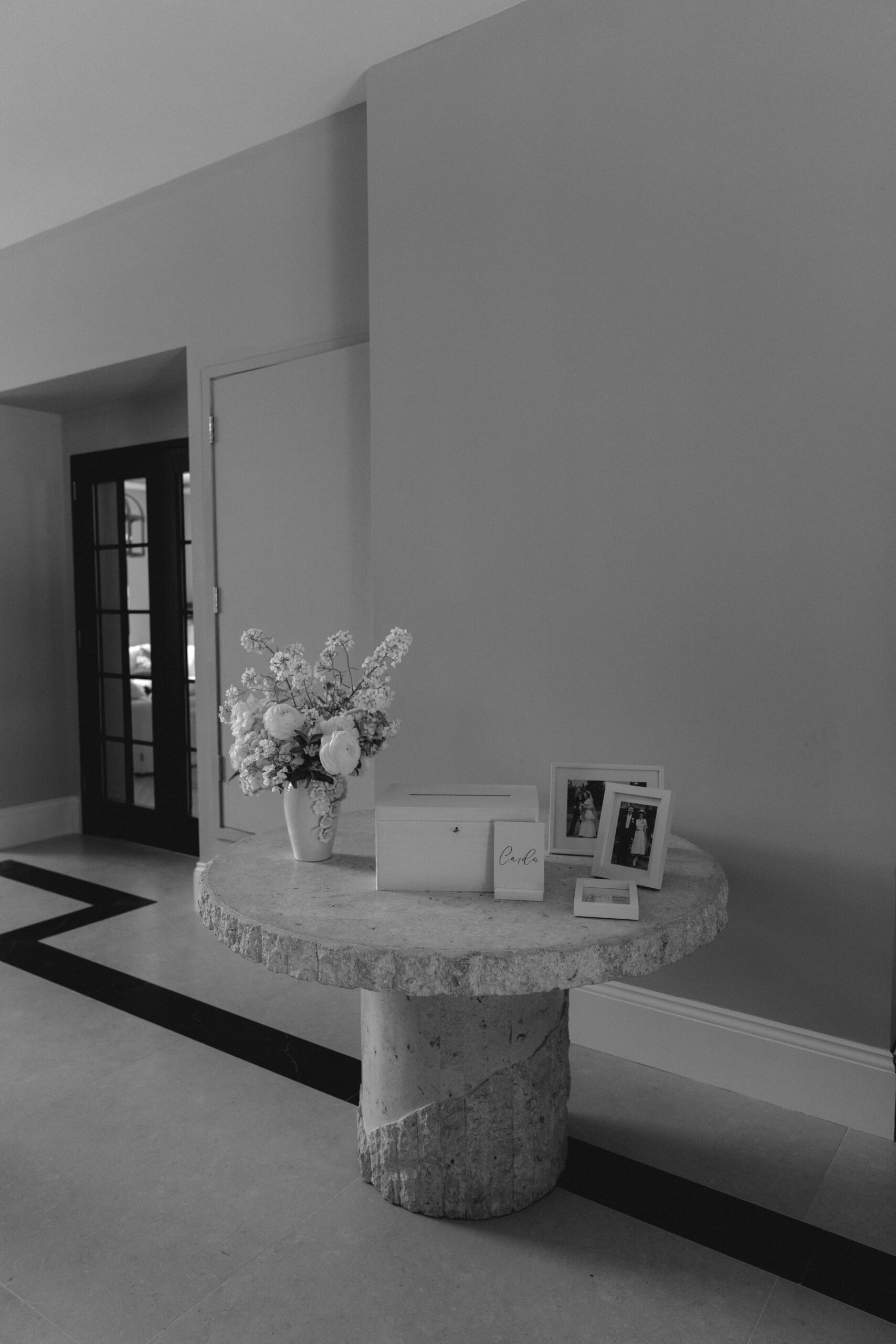 WEDDING-PLANNER-COTSWOLDS A black and white image of an entrance table for a wedding with card box and florals on a stone top table.