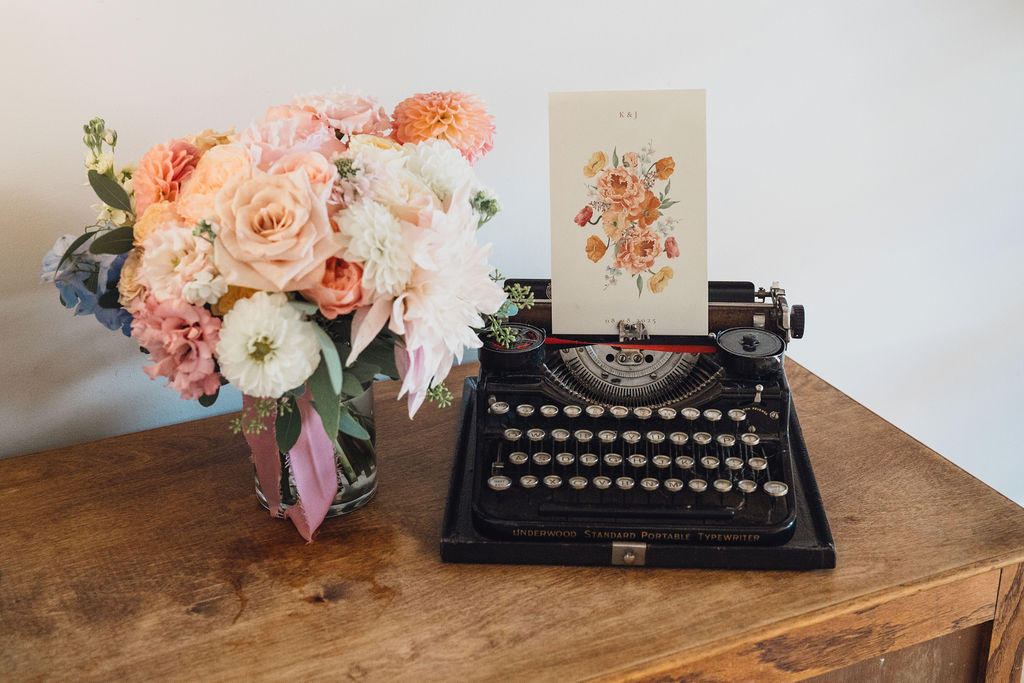 A colour image of an old-fashioned typewriter with  a summer wedding bridal bouquet and wedding invitation.