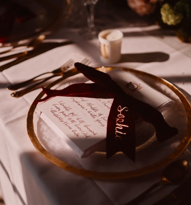 A colour image of an autumn wedding place setting with hand calligraphy menu and a red velvet bow by Soiree Studio at Hedsor House.