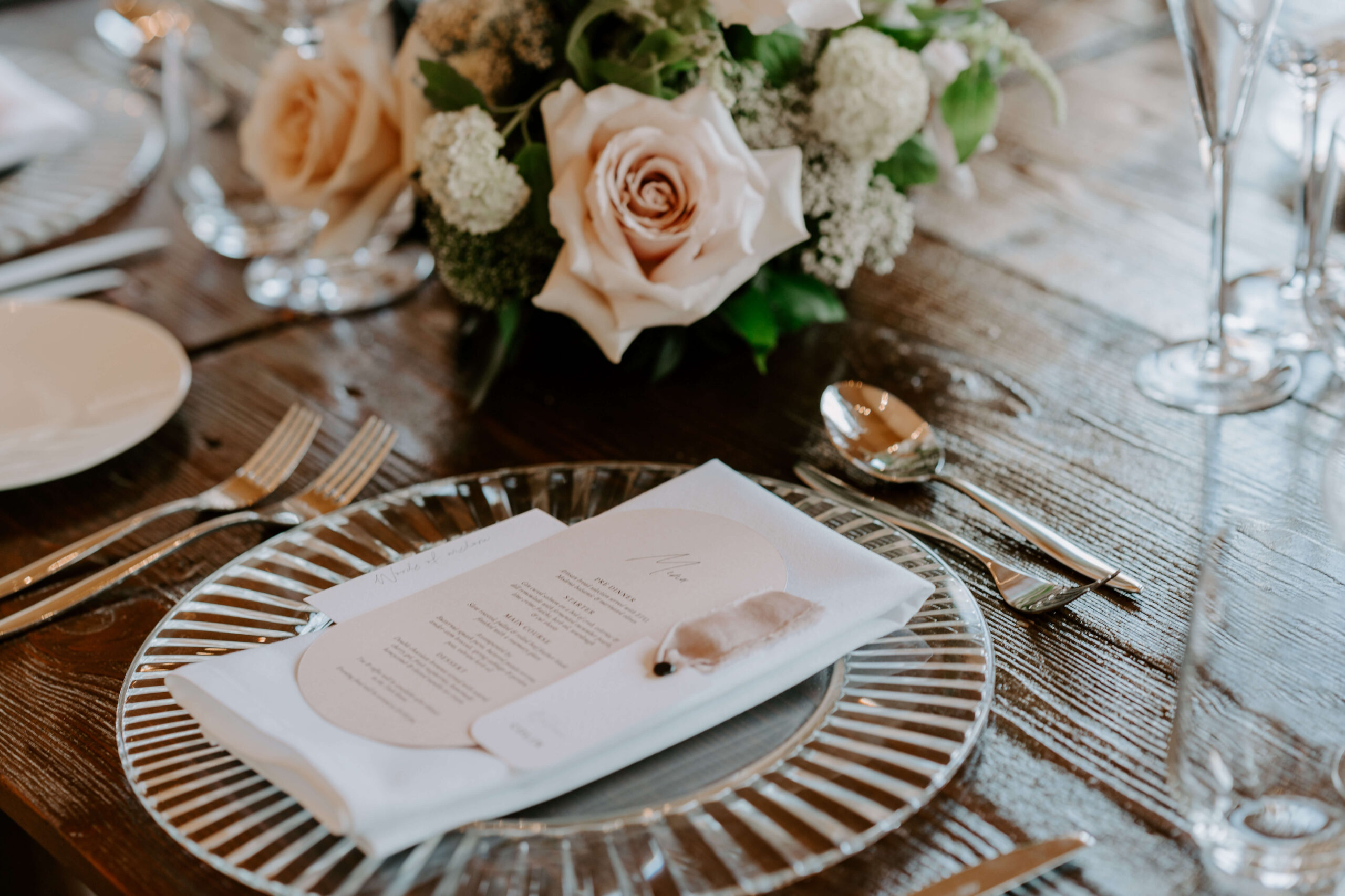 bespoke-wedding-design-and-planning-cotswolds A colour image of a wedding table setting on wooden tables with blush flowers and pink table stationery by Soiree Studio.