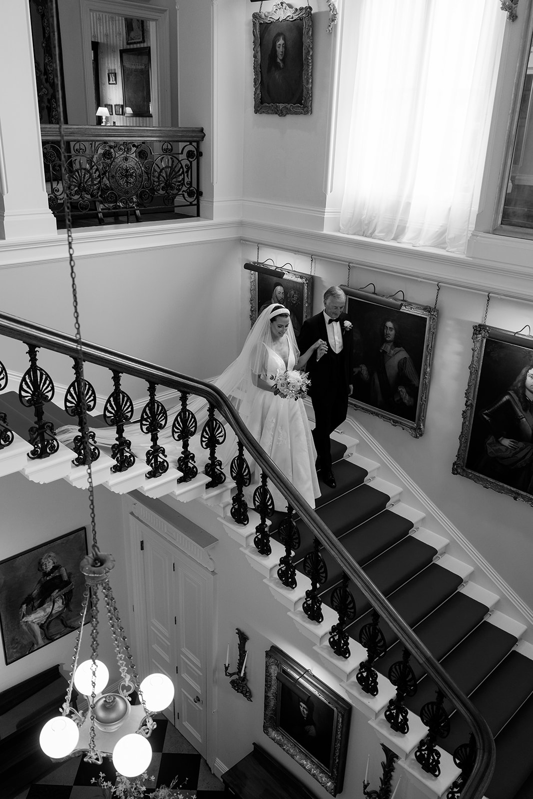 Madeleine & Chris A black and white image of a bride walking down the stairs of Capesthorne Hall in Cheshire to her ceremony