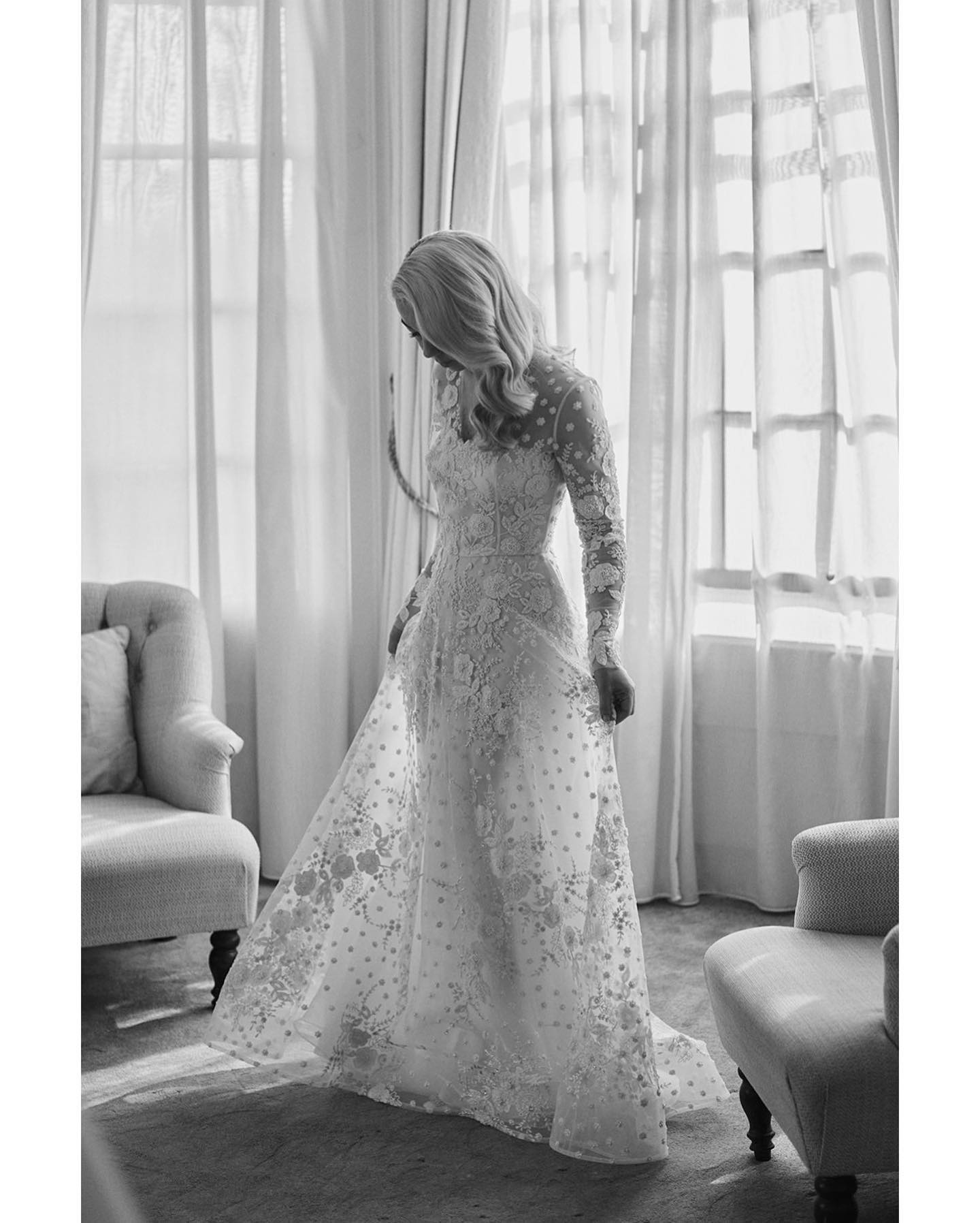 A black and white image of a bride in her lace wedding dress in front of a window at Hedsor House.