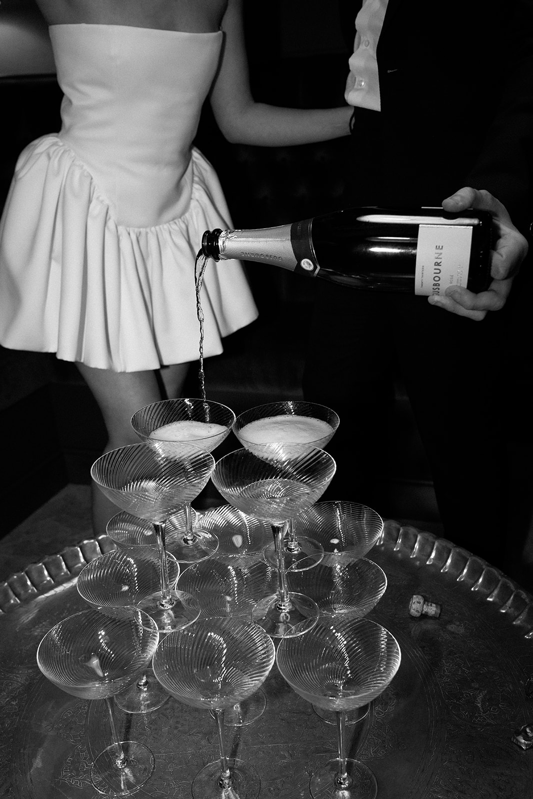 Birdsall House A black and white image of a bride and groom pouring champagne onto a champagne tower at their marquee wedding in the Cotswolds.