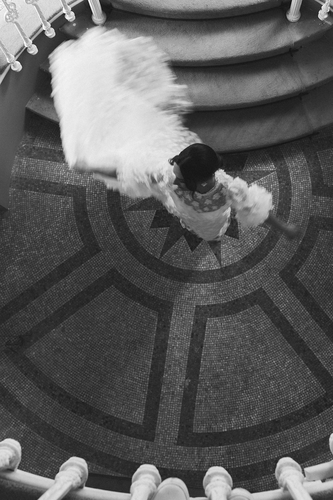 A black and white image of a bride twirling around in her dress at the bottom of the stairs at Hawkstone Hall.
