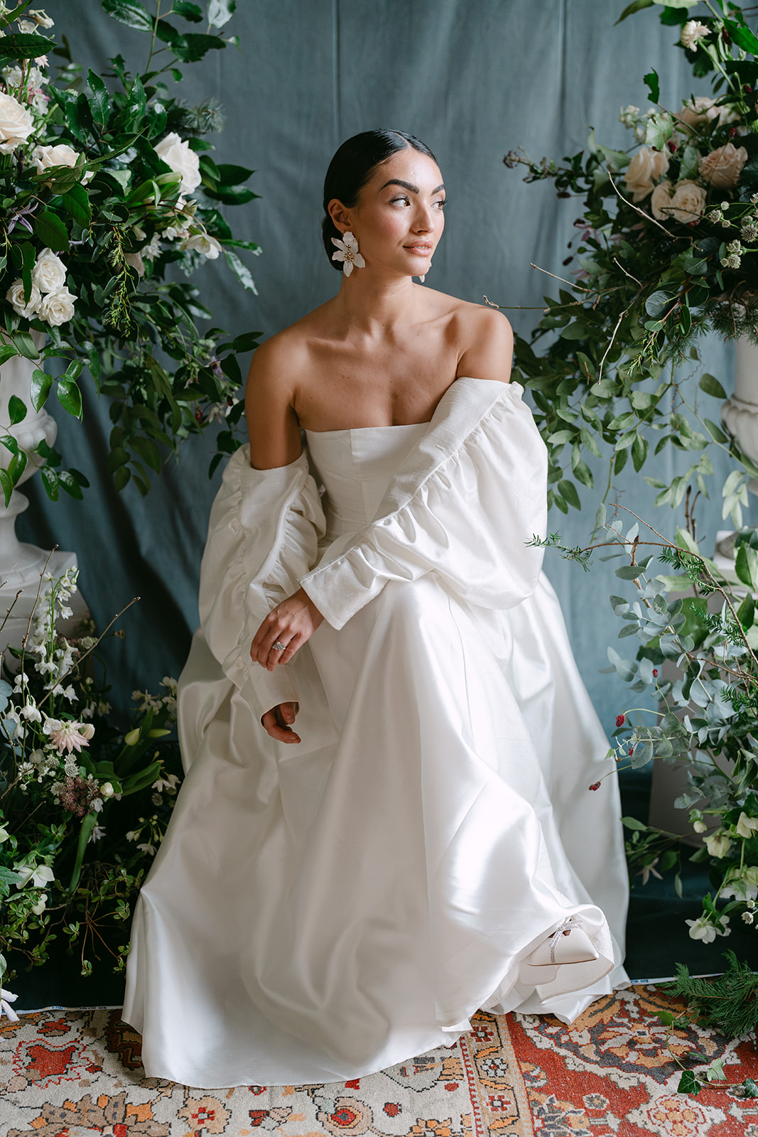 Birdsall House A colour image of a bride sitting in her wedding dress with fresh flowers around her at a marquee wedding planned by Soiree Studio.