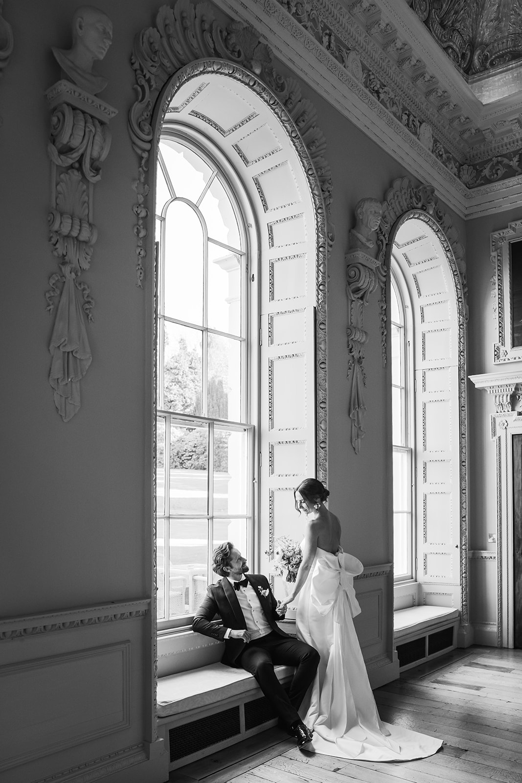 A black and white image of a bride and groom sat in the grand windows of Hawkstone Hall after a wedding planned by soiree studio.