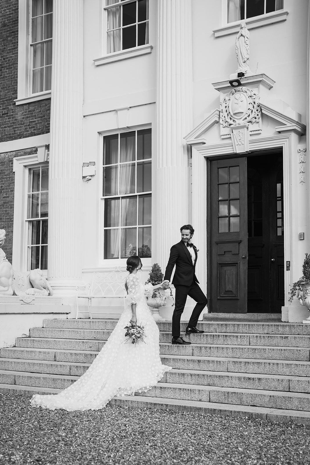 A black and white image of a bride and groom entering Hawkstone hall after their wedding ceremony planned by Soiree Studio.