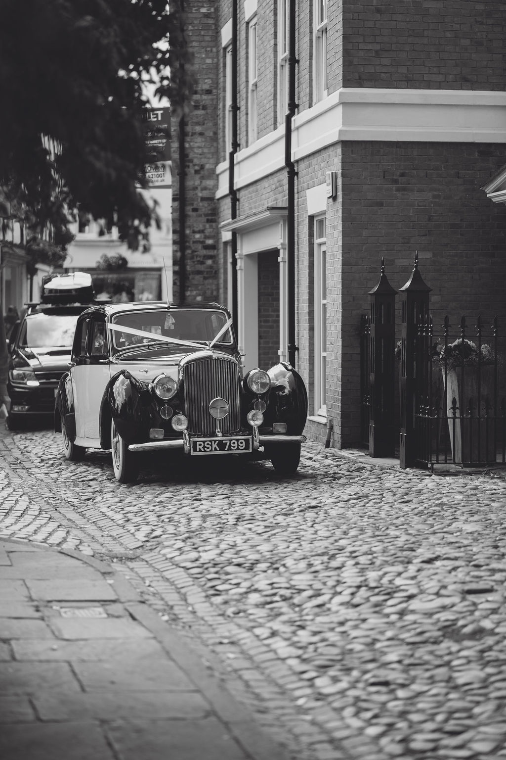 luxury-vintage-car-hire-wedding-planner-shropshire A black and white image of a luxury vintage Morgan wedding car arriving at Nantwich church for a wedding planned by Soiree Studio.