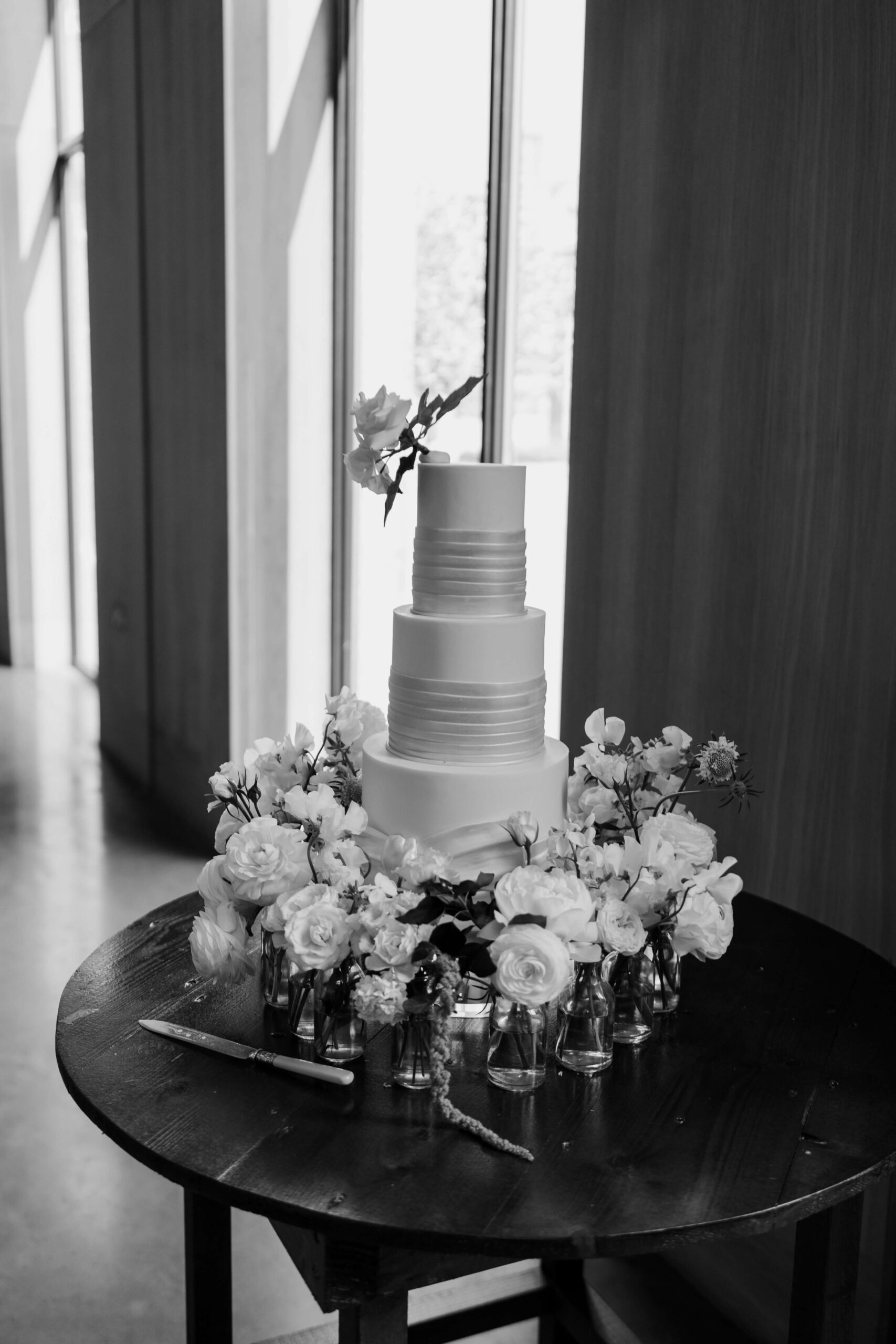 luxury-wedding-cake-wedding-planner-dorfold-hall-cheshire A black and white image of a sleek, minimal 3 tiered wedding cake by The Frostery with fresh flowers at the base.