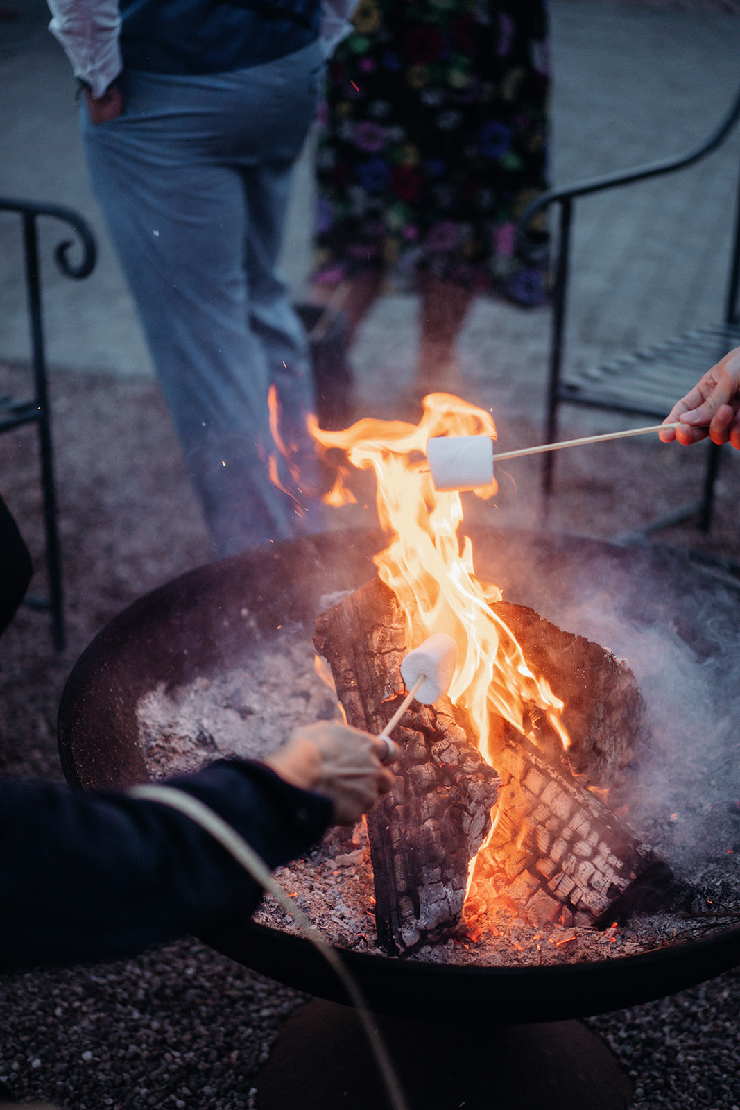 Amy and Jack A colour image of wedding guests enjoying toasting marshmallows over a fire pit at a wedding planned at Dorfold Hall in Cheshire.