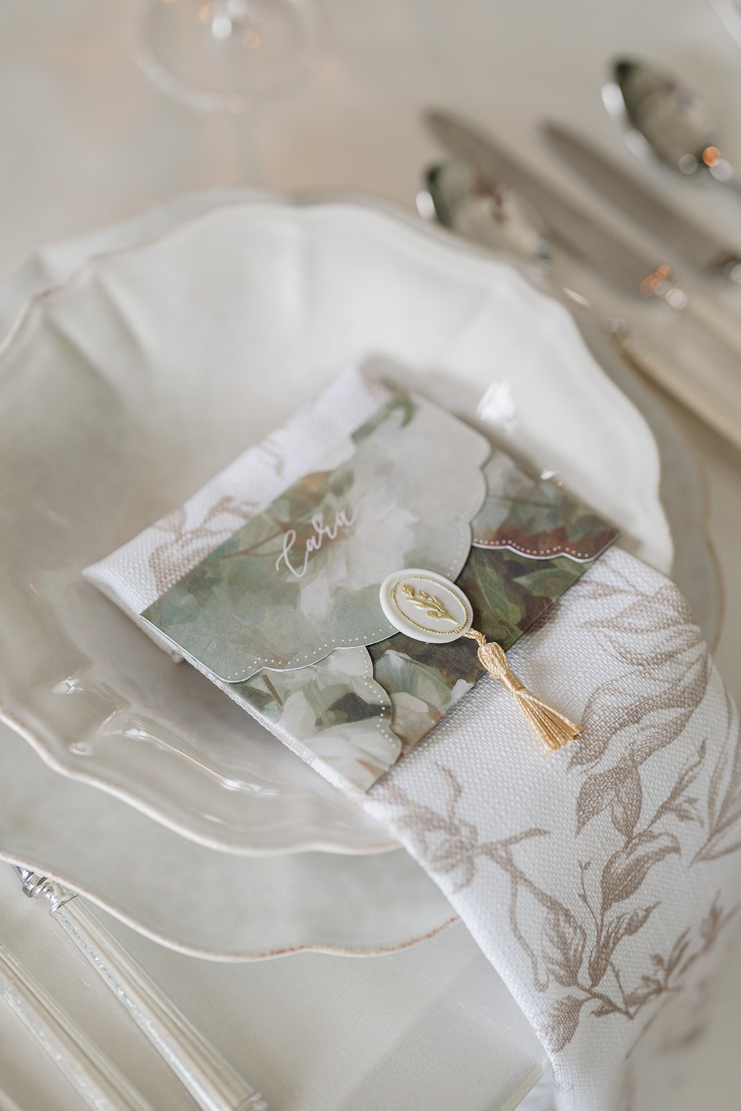 Birdsall House A colour image of a wedding place setting with fine china, a neutral floral napkin and envelope style place card.