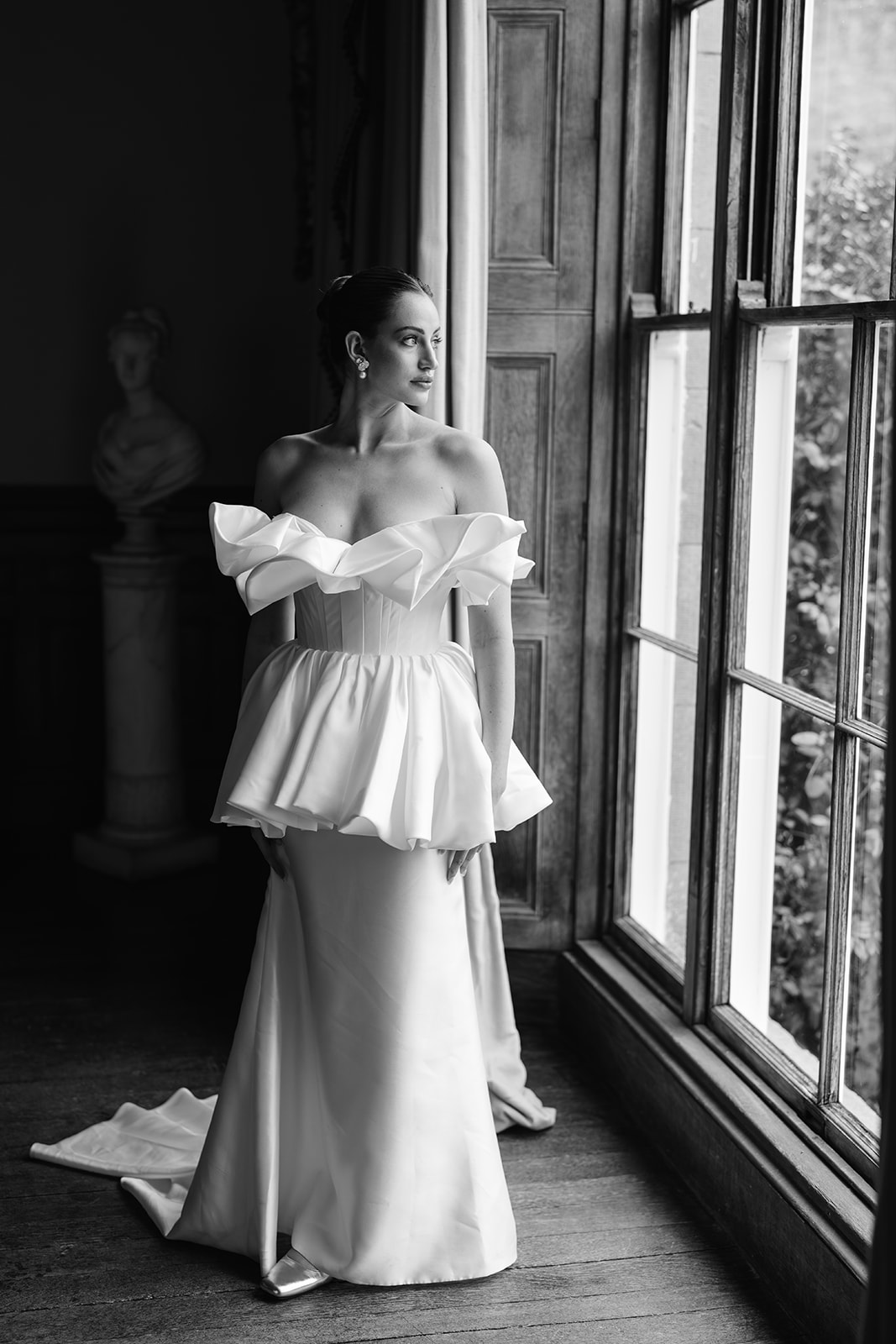 Birdsall House A black and white image of a luxury planned wedding at Birdsall House in Yorkshire with the bride in her dress looking out of the grand windows.