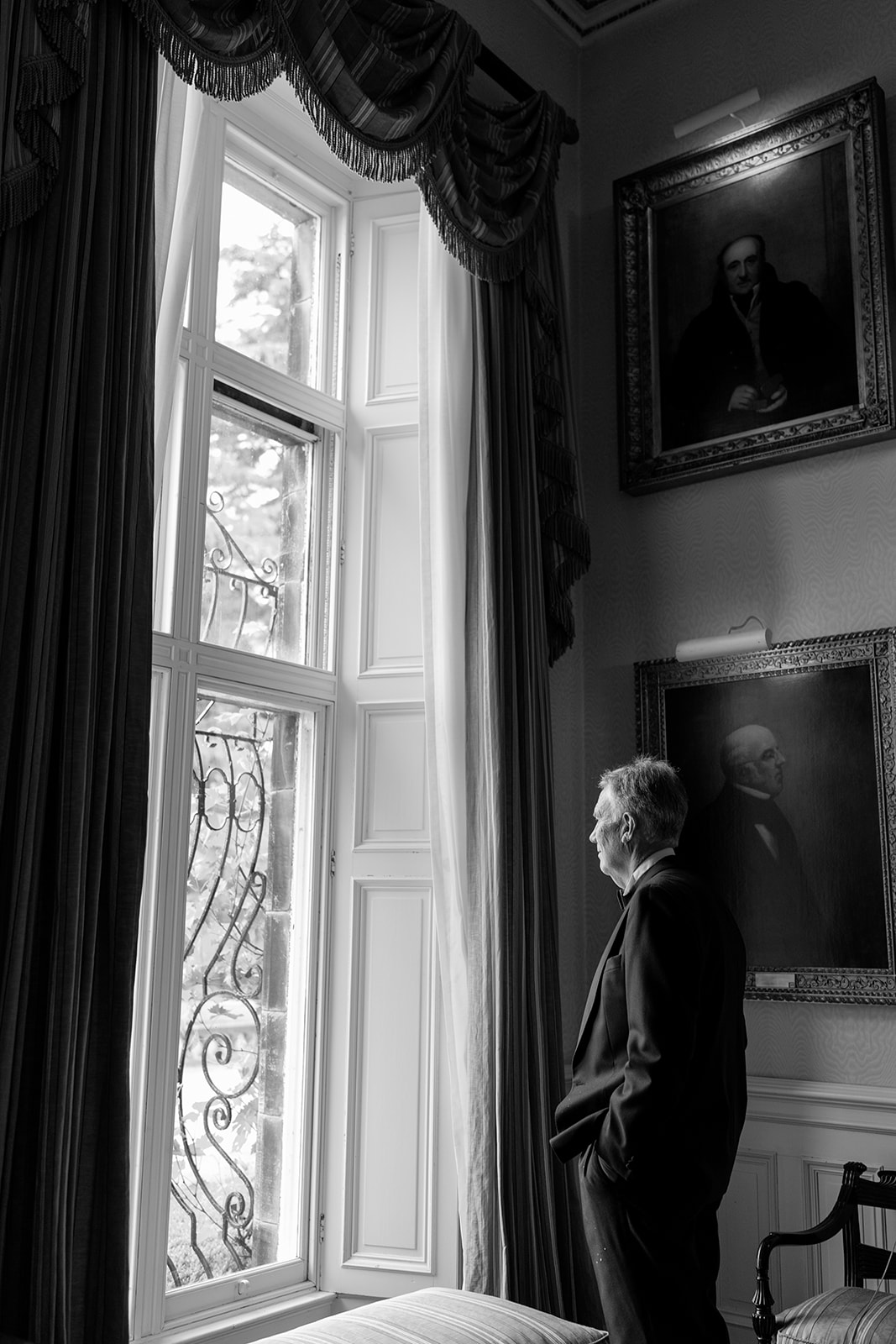 Madeleine & Chris A black and white image of a wedding guest having a quiet moment looking out on the grounds of Capesthorne Hall in Cheshire.