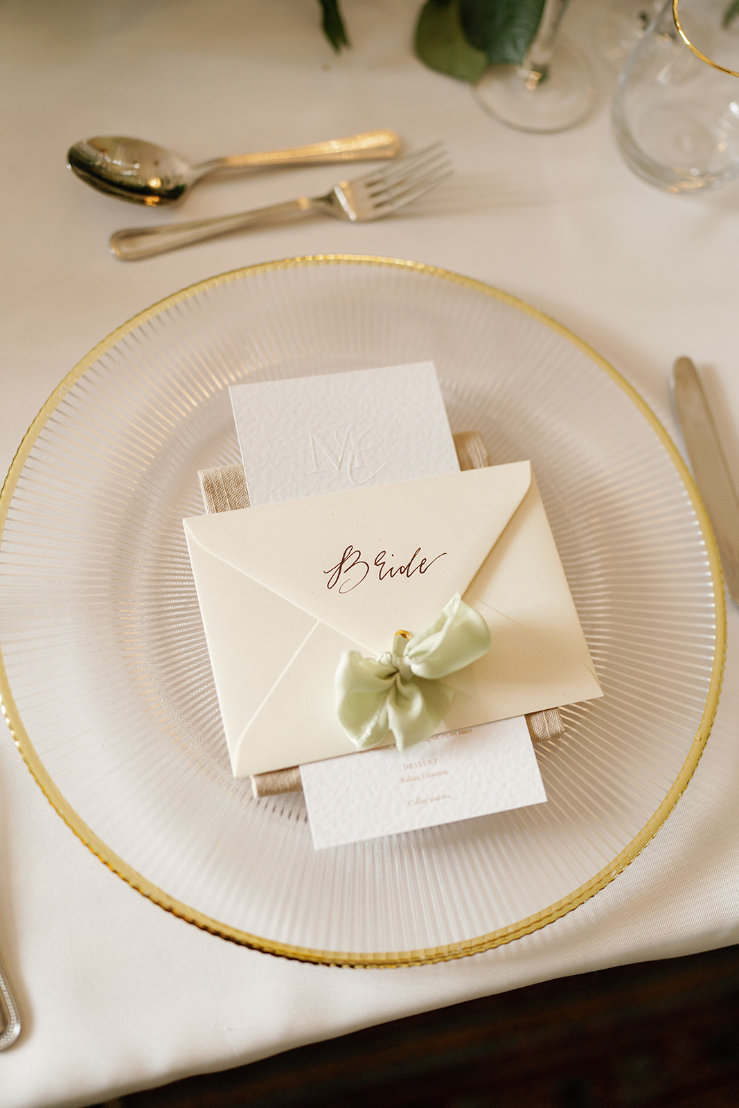 Madeleine & Chris A colour image of a wedding place setting created by soiree studio with a sage green bow.