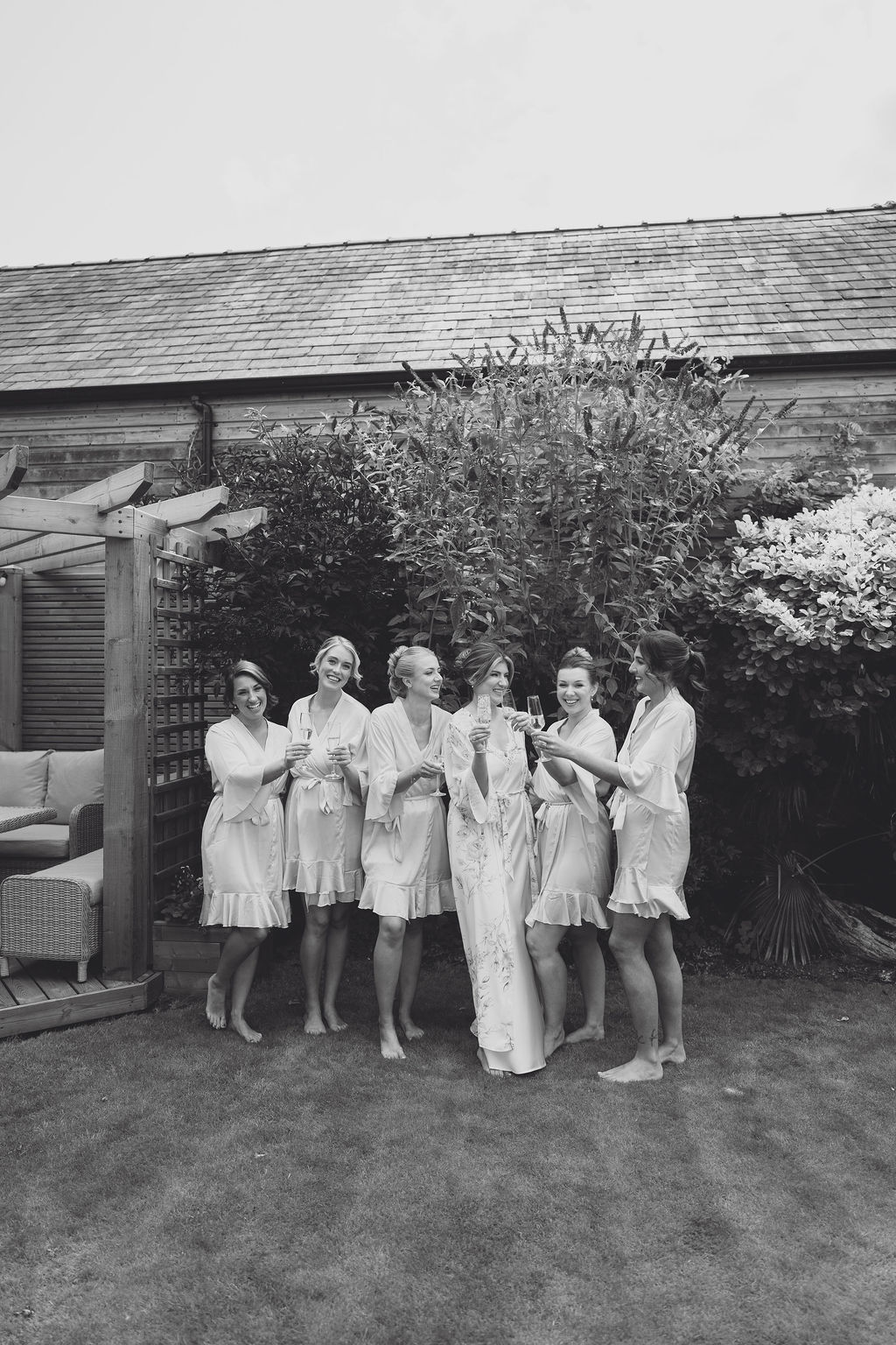 A black and white image of a bridal party in their dressing gowns enjoying getting ready with champagne.