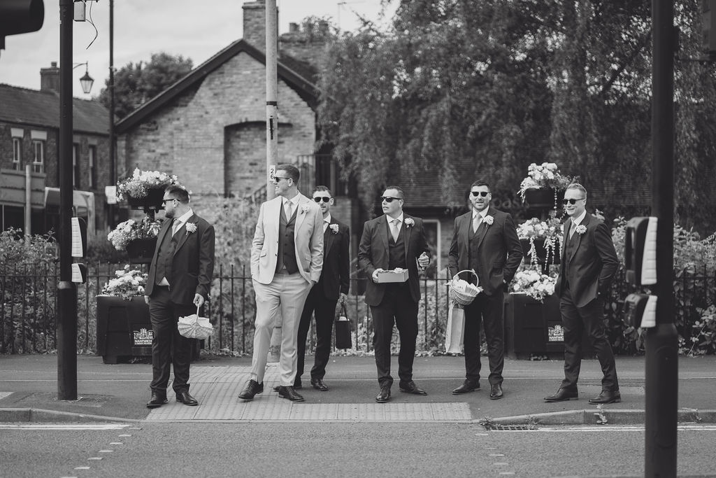 A black and white image of groomsmen crossing the road on the way to the church in Nantwich.