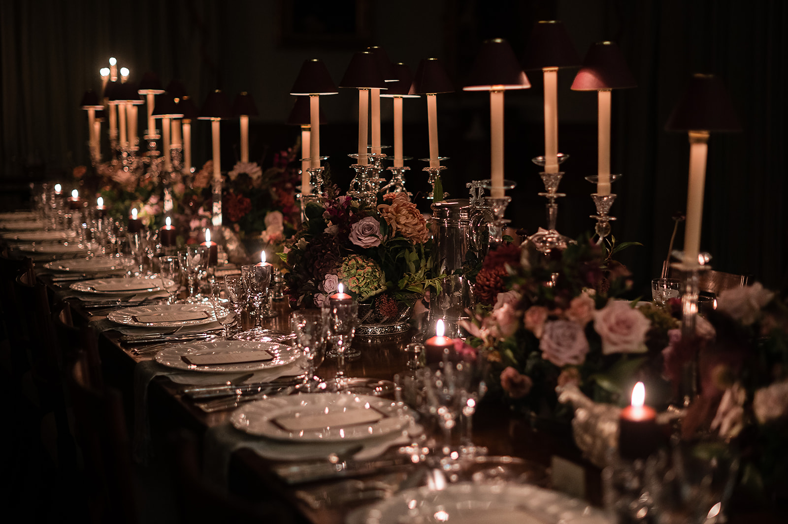 A colour image of a long dining table with an abundance of candlelight for a private dinner at Birdsall house planned by UK wedding planner Soiree Studio.