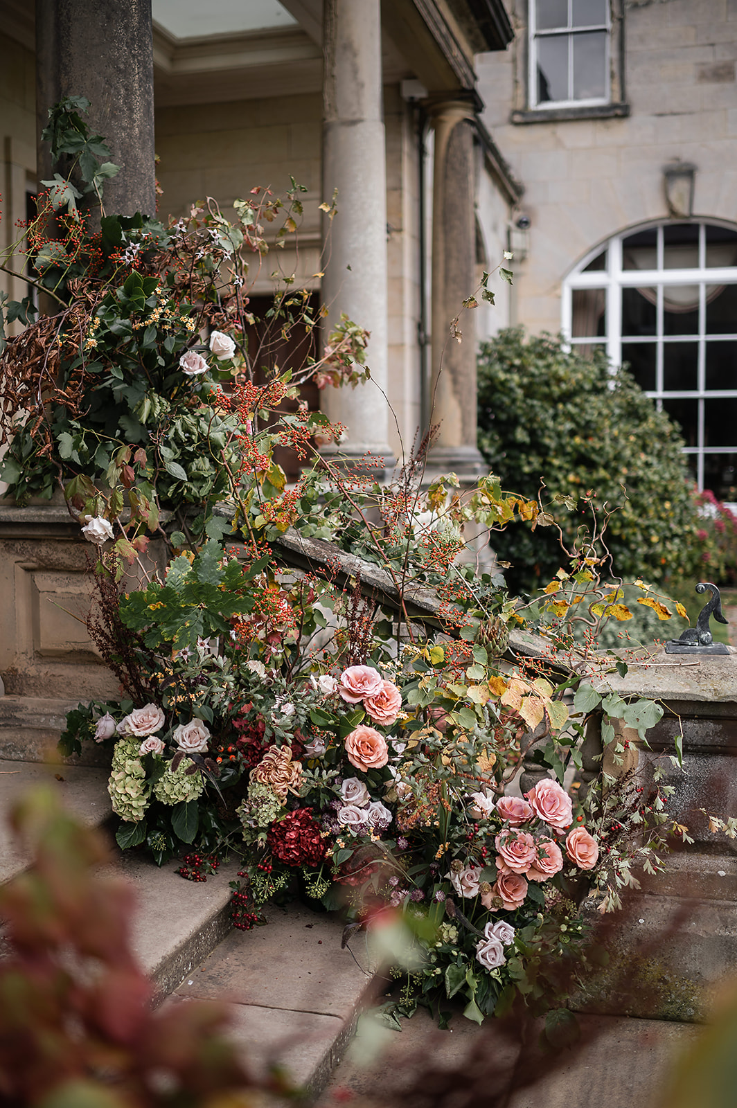 A colour image of autumnal wedding flowers on the steps to the entrance of Birdsall House Wedding Venue in the UK.