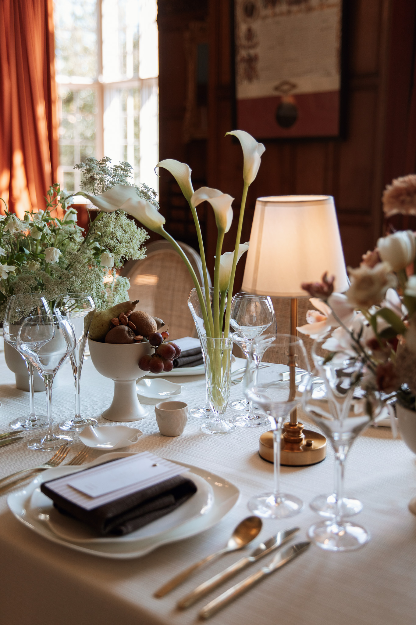 A colour image of a wedding dining table with neutral lamps and calla lilies at Arley Hall Cheshire.