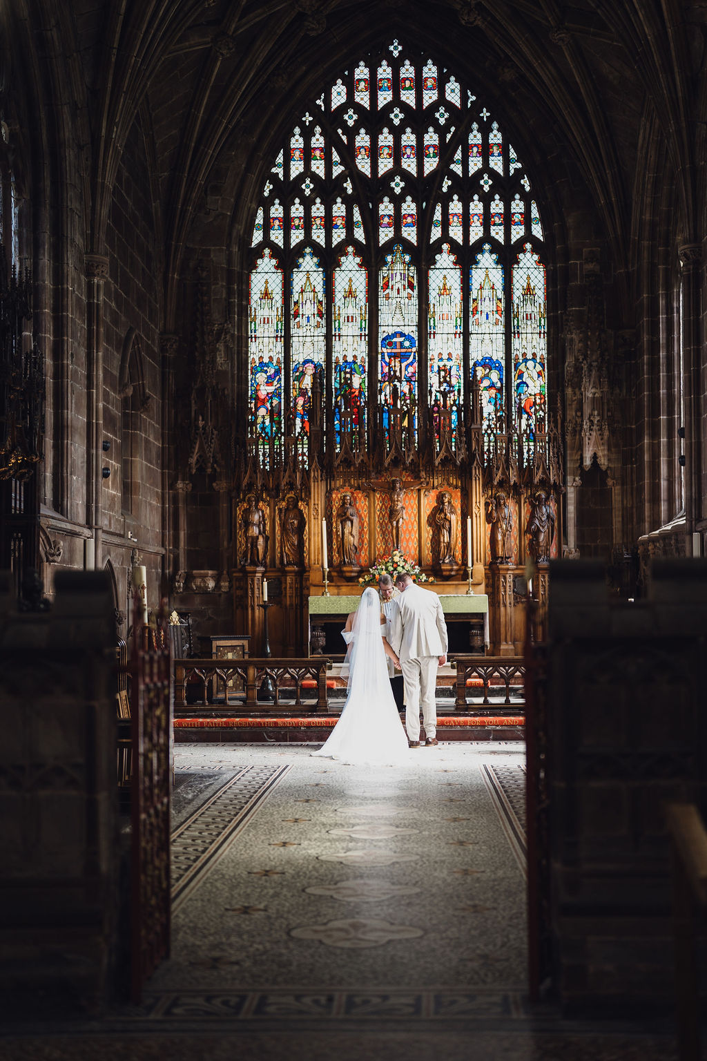 A colour image of a bride and groom at the altar of their local church in Nantwich reading their wedding vows, with the summer light hitting them  beautifully. 