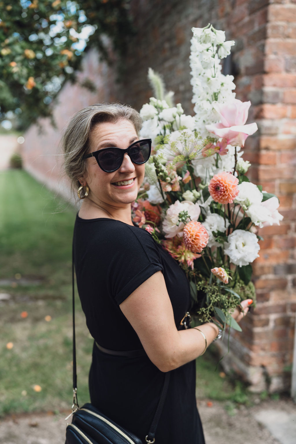 A colour image of Soirée Studio founder Corrie McDonald, carrying a large summer floral arrangement at a marquee wedding in Shropshire. 