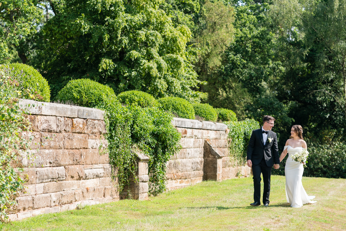 A colour image of a bride and groom walking in the grounds of Hampton Manor UK wedding venue.