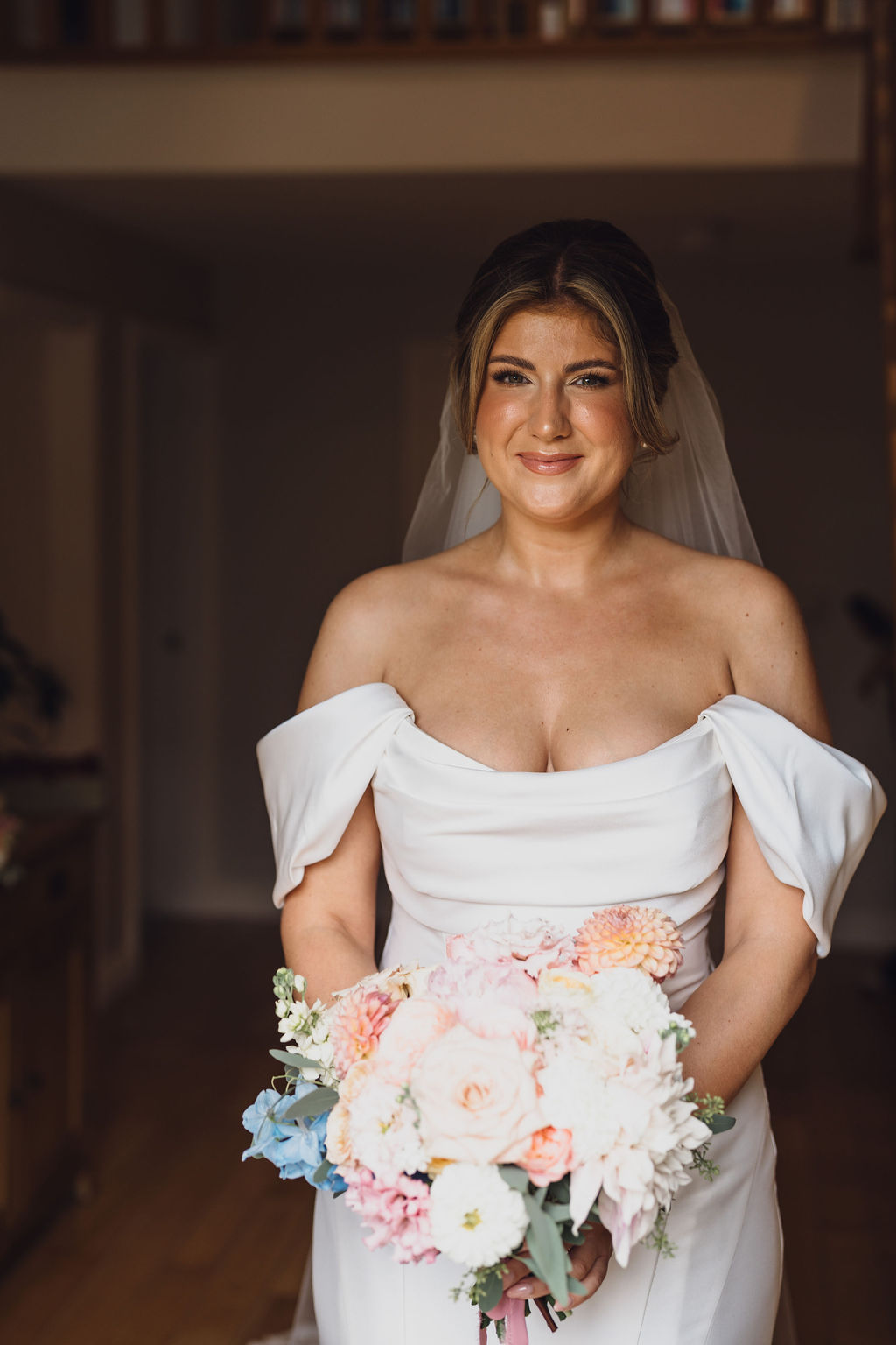 A colour image of a beautifully happy bride with her summer pastel wedding bouquet on the morning of her wedding at Combermere Abbey Shropshire.