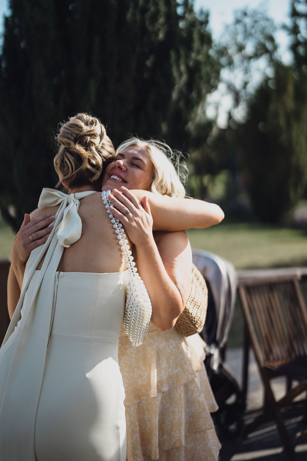 A colour image of a bride hugging one of her guests in the summer sunshine at Comberemere Abbey Shropshire.